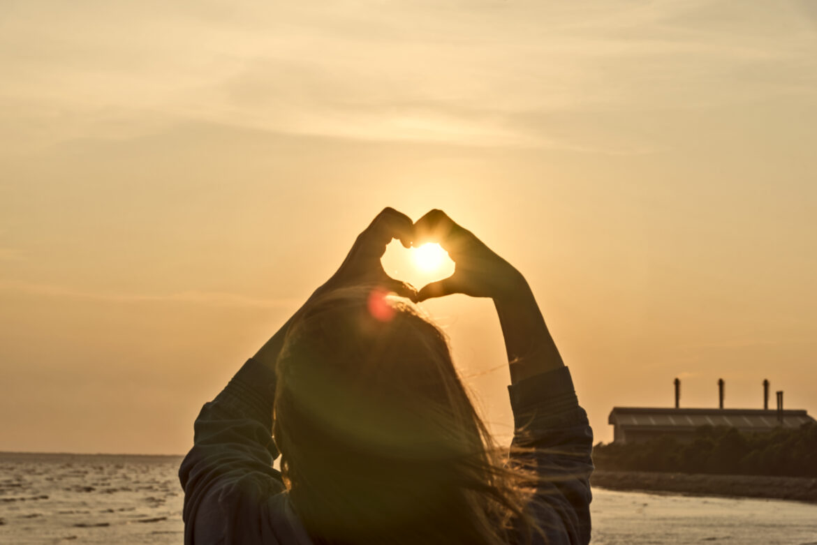 hands forming a heart shape with sunset silhouette