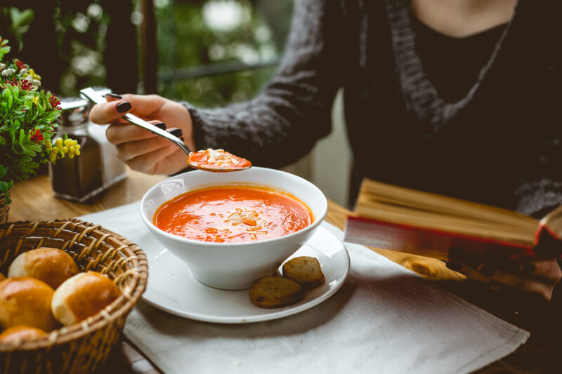 side view of a woman eating tomato soup with toasts at the table
